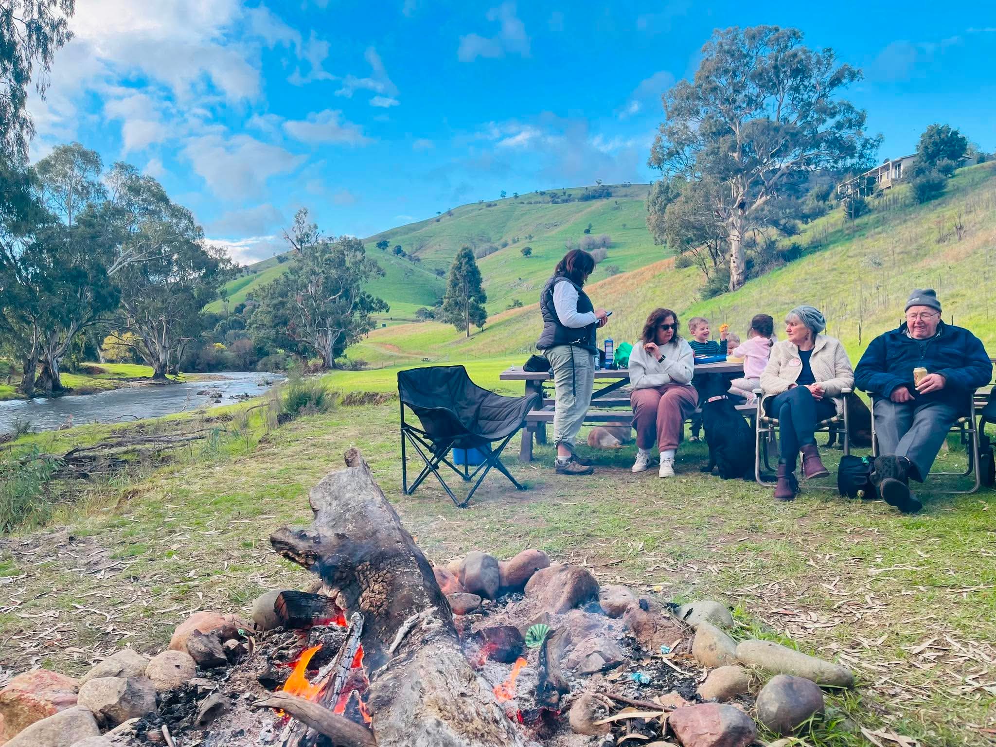 Family gathered by the campfire at the river's edge at Elm Cottage